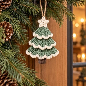 Crochet Christmas tree ornament used as a festive napkin decoration on a neutral holiday table setting with pine greenery and warm Christmas lights.

Handmade sage green crochet Christmas tree ornament hanging from a wooden door knob beside evergreen garland and pinecones in a cozy holiday entryway.

Three layered crochet Christmas tree ornaments hanging from a natural branch near a bright window with soft Scandinavian Christmas home decor.