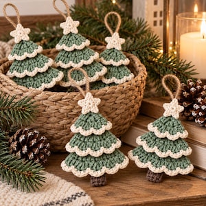 Handmade sage green crochet Christmas tree ornaments with cream scalloped edging, white crochet stars, brown trunks, and hanging loops displayed on a rustic wooden table.

Layered crochet Christmas tree ornaments hanging on an evergreen Christmas tree with warm fairy lights and cozy holiday decorations in the background.

Crochet Christmas tree garland with sage green layered trees, cream scalloped borders, white stars, and brown trunks decorating a rustic fireplace mantel.