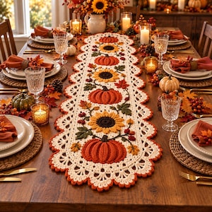 May include: A long, rectangular crochet table runner featuring a repeating pattern of orange pumpkins and yellow sunflowers with green leaves, bordered by a cream-colored scalloped edge. The runner is centered on a wooden dining table with place settings.