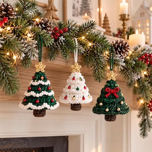 May include: Three crocheted Christmas tree ornaments hanging from a garland. Two trees are dark green with red and gold beads and a gold star topper. One tree is cream-colored with red and green beads and a gold star topper.
