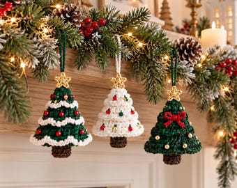 May include: Three crocheted Christmas tree ornaments hanging from a garland. Two trees are dark green with red and gold beads and a gold star topper. One tree is cream-colored with red and green beads and a gold star topper.