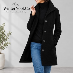 May include: A black mid-length coat featuring a high collar, long sleeves, and a front button closure. The coat is worn over a black turtleneck sweater and blue denim jeans. The WinterNookCo logo is visible in the upper left corner.