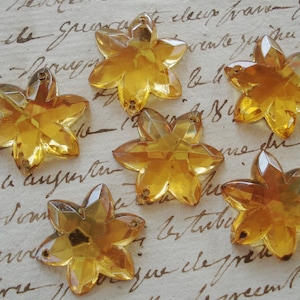 May include: Six amber glass star-shaped embellishments with a faceted design. The embellishments are scattered on a piece of paper with handwritten text.