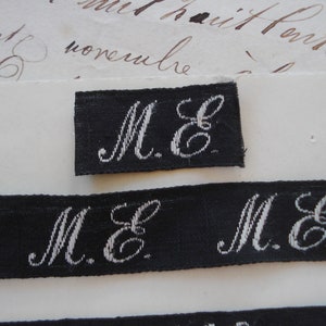 May include: Close-up of a black fabric label with white embroidered letters "M.E."