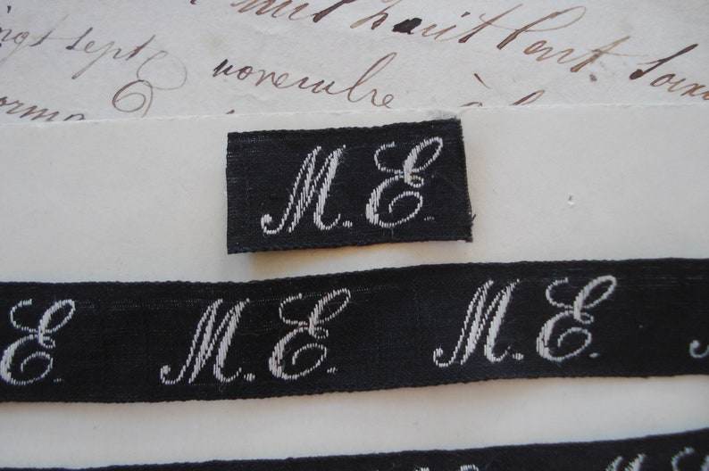 May include: Close-up of a black fabric label with white embroidered letters "M.E."
