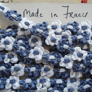 May include: White and blue floral trim ribbon. The ribbon is made of a soft, delicate fabric and features a repeating pattern of small flowers. The ribbon is labeled "Made in France".