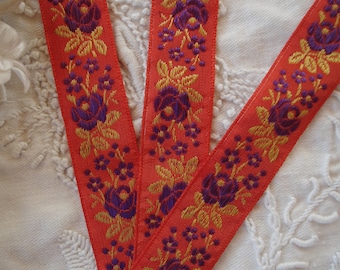 May include: Three pieces of orange ribbon with a gold and purple floral pattern. The ribbon is woven with a repeating pattern of flowers and leaves.
