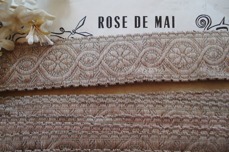 Puede incluir: Dos piezas de ribete beige con un patr&oacute;n tejido. La pieza superior tiene un dise&ntilde;o m&aacute;s intrincado con un motivo floral repetitivo. La pieza inferior tiene un dise&ntilde;o m&aacute;s simple y texturizado. El texto "ROSE DE MAI" es visible en el fondo.