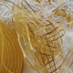 May include: A roll of gold ribbon with a gold mesh ribbon on top. The ribbon is on a white lace surface.