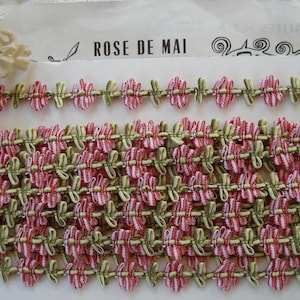May include: Close-up of decorative trim with a floral design. The trim features a repeating pattern of red and white flowers with green accents. The text "ROSE DE MAI" is visible on the background.