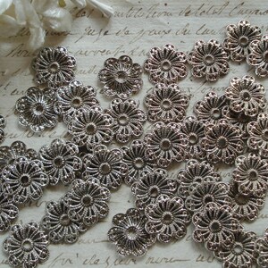 May include: A collection of silver metal filigree embellishments in the shape of flowers. The embellishments are delicate and intricate, with a floral design.