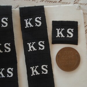 May include: Five black fabric labels with white embroidered letters spelling "KS".