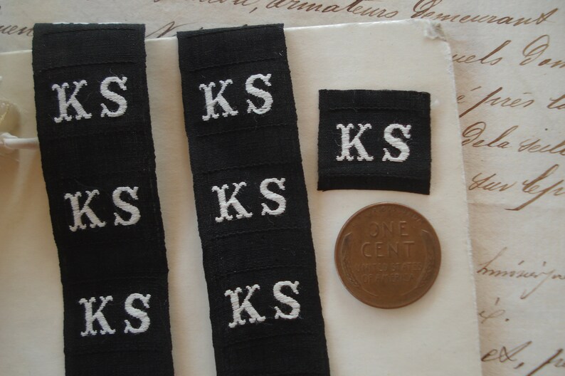 May include: Five black fabric labels with white embroidered letters spelling "KS".