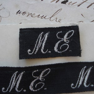 May include: Close-up of a black fabric label with white embroidered letters "M.E."