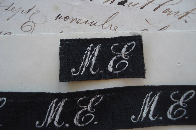 May include: Close-up of a black fabric label with white embroidered letters "M.E."