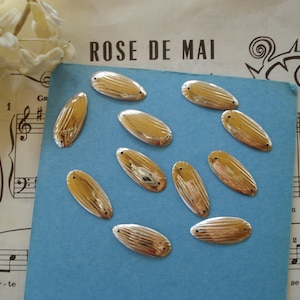 May include: Ten gold-colored oval-shaped sequins with a ribbed texture. The sequins are scattered on a blue surface.