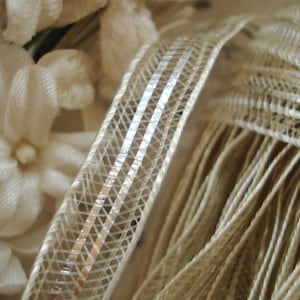 May include: Close-up of a white, delicate, woven fabric with a subtle shimmer. The fabric has a delicate, open weave pattern and a soft, flowing texture.