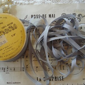 May include: A spool of 1/4 inch wide gray rayon ribbon. The spool is labeled "Ribbons" and has the text "100 Yards Gauge 4 1/2 sts #1" printed on it.