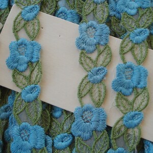 May include: Blue and green floral lace trim with a delicate floral pattern. The trim features small blue flowers with green leaves.