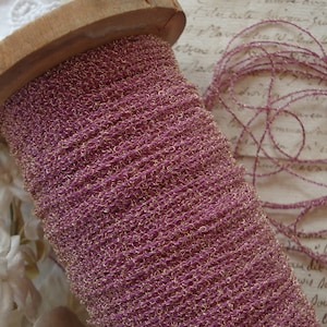 May include: A spool of pink and gold metallic thread. The thread is wound around a wooden spool.
