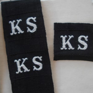 May include: Three black fabric labels with white embroidered letters spelling "KS".