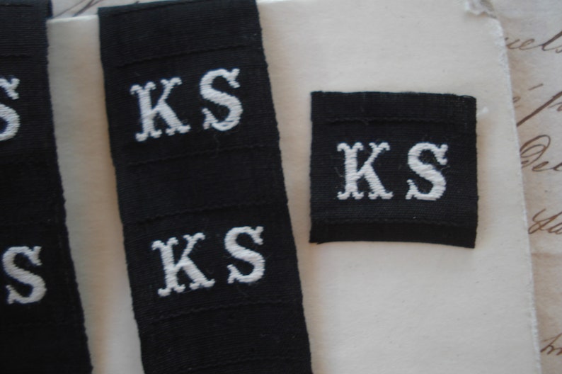 May include: Three black fabric labels with white embroidered letters spelling "KS".