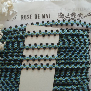 May include: Black, blue, and green trim with a repeating pattern. The trim is on a white background with the text "ROSE DE MAI" printed on it.