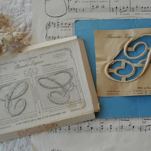 May include: A vintage embroidery pattern booklet with the title "Planchetis-Express" and a close-up of a decorative "F" letter embroidery pattern. The booklet is made in France and includes instructions for embroidery.