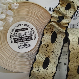 May include: A spool of beige ribbon with black polka dots. The ribbon is rolled up and has a label that reads "Just Beautiful Ribbons, Quality Controlled Fashion Colored, Since 1900, For Those Who Care and Know the Difference, Exclusively at Hendler's, 47 W. 34th St. N.Y.C."