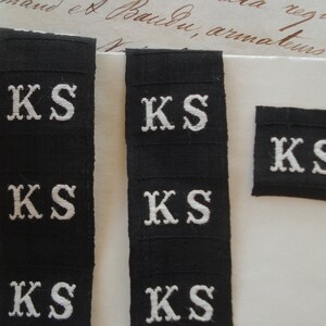 May include: Five black fabric labels with white embroidered letters spelling "KS".