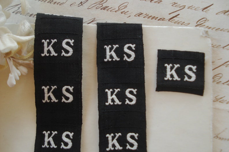 May include: Five black fabric labels with white embroidered letters spelling "KS".