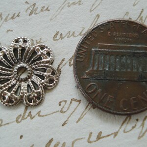 May include: A silver filigree flower charm with a hole in the center. The charm is about the size of a US penny.