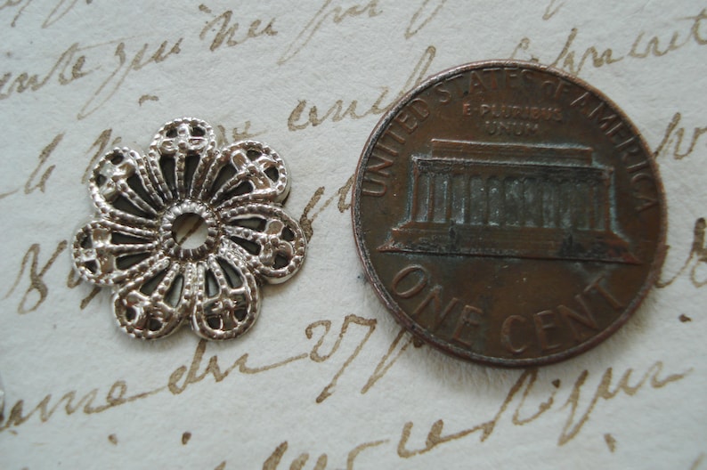 May include: A silver filigree flower charm with a hole in the center. The charm is about the size of a US penny.