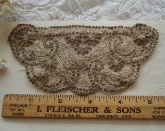 May include: A delicate, off-white lace trim with a brown embroidered design. The trim has a scalloped edge and is perfect for adding a touch of elegance to any project.