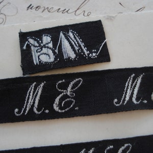 May include: A black fabric label with white embroidered letters "M.E." and a small black fabric label with a white embroidered image of two shoes.