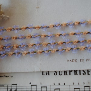 May include: Four strands of lavender and peach colored trim with a floral design. The trim is made in France and is labeled "La Surprise".