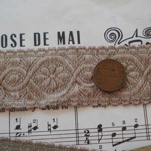 Puede incluir: Un primer plano de un ribete de tela con estampado marr&oacute;n y beige con una moneda de un centavo encima. La tela tiene un dise&ntilde;o tejido y un borde festoneado. La moneda es de color cobre y tiene las palabras "ONE CENT" inscritas en ella.