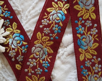 May include: Red ribbon trim with a floral pattern in gold, blue, and silver. The flowers are roses and smaller blossoms.