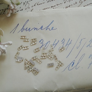 May include: A close-up of a white envelope with blue handwriting. The envelope contains a bunch of small, clear, rectangular rhinestones. The handwriting says "1 bunche 30434/5/2 in. cl. f."