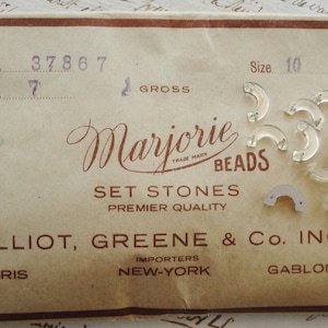 May include: A vintage packaging card for Marjorie Beads Set Stones, Premier Quality. The card features the company name, address, and a trademarked logo. The card also includes a size 10 label and a number 37867 label. The card is decorated with a variety of clear glass beads.