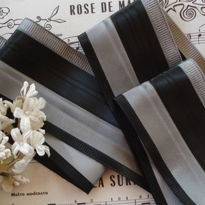 May include: Black and silver striped ribbon with a satin finish. The ribbon is folded and arranged on a sheet of music.