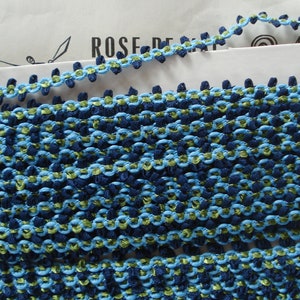 Op de afbeelding: Blauwe en groene trim met een herhalend patroon van kleine pompoentjes. De trim is gemaakt van een zachte, geweven stof.