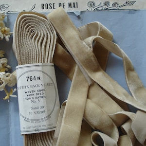 Könnte beinhalten: Eine Rolle mit 9,14 Metern beigefarbenem, gewebtem, 100 % Rayon-Faille-Rückseiten-Samtband. Das Etikett lautet "764 N Faille Back Velvet Woven Edge Yarn Dyed 100% Rayon No. 5 Sand 39 10 Yards Made in Switzerland Registration RN 18107".