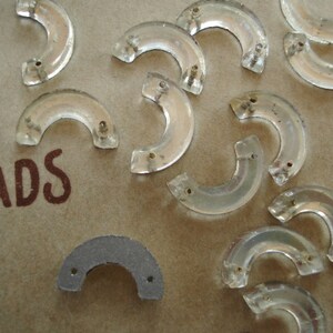 May include: A collection of clear glass beads in the shape of a crescent moon. The beads are arranged on a brown surface with the word "BEADS" printed on it.