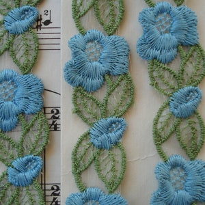 May include: Three pieces of blue and green floral lace trim. The lace is made of a sheer fabric with embroidered flowers and leaves.