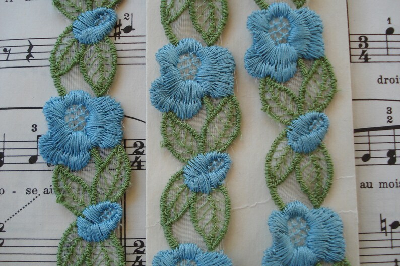 May include: Three pieces of blue and green floral lace trim. The lace is made of a sheer fabric with embroidered flowers and leaves.