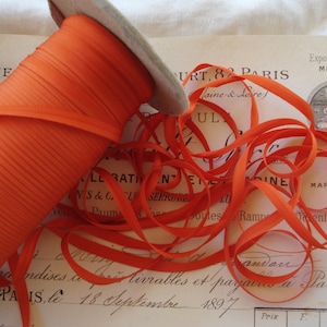 以下が含まれることがあります： 「URT, 82 PARIS」と「Exposition Univ de Paris 1889 MEDAILLE D'ARGENT」と書かれたビンテージラベルが付いた、明るいオレンジ色のリボン巻き。