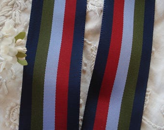 Puede incluir: Primer plano de una cinta rayada con rayas azul marino, verde oliva, azul claro y rojo. La cinta está sobre un fondo blanco.