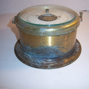 May include: Antique brass barometer with a glass face. The face displays weather indicators and a needle. The brass casing shows signs of age and wear. The barometer is a vintage nautical instrument.