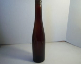 May include: A tall, brown glass bottle with a narrow neck and a rounded base. The bottle has a smooth, glossy surface and is empty. The bottle is likely for storing liquids.
